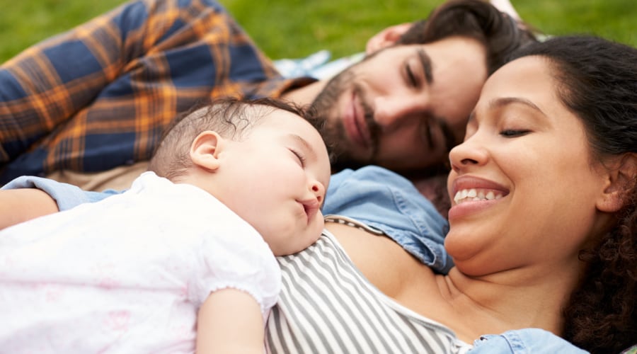 New parents lay in the park with their infant