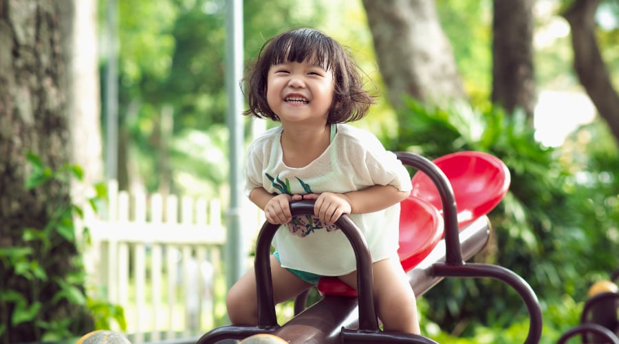 A young Asian girl riding on playground equipment