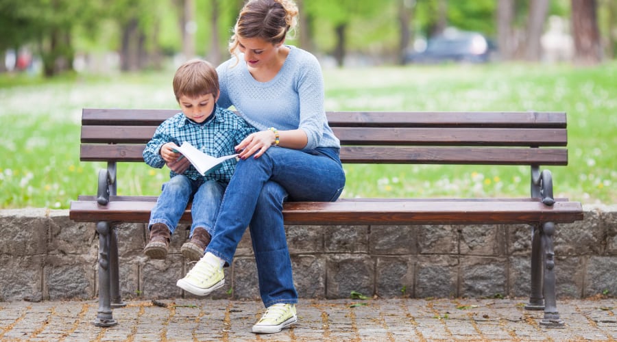 A mother reads with her son on a park bench