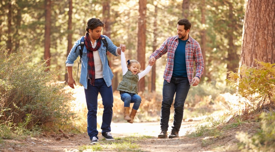 Two fathers walk in the woods with their daughter