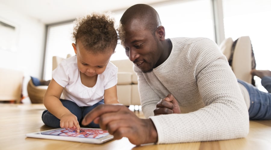 A father uses a digital tablet with his toddler