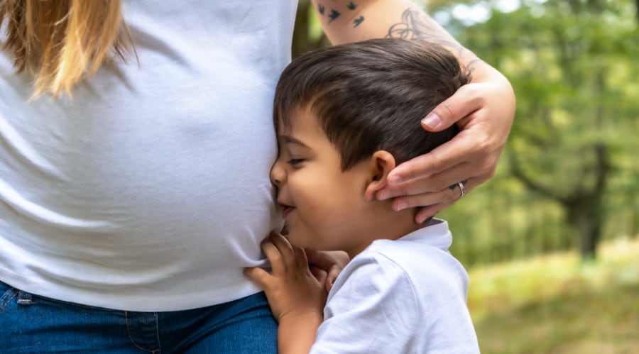 A young boy presses his face against his pregnant mother's side