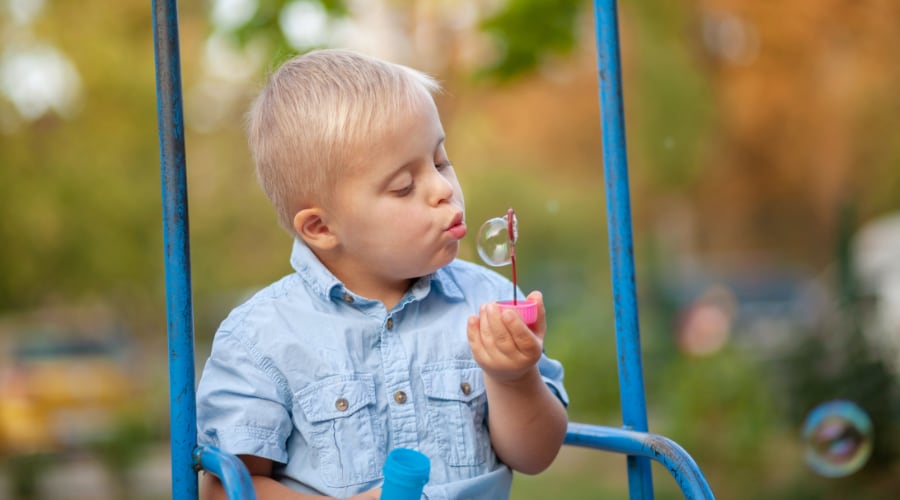 A young boy with Down Syndrome rides on a swing and blows soap bubbles