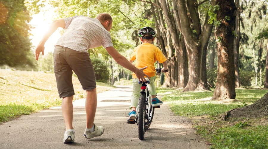 Adventure Pediatrics A dad in the park with his son, teaching him how to ride a bike